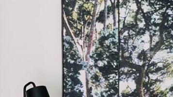 A bedroom with a bed, a black floor lamp, and a wall with a forest print.