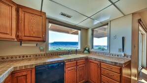 Una cocina con armarios de madera, lavavajillas, fregadero y ventanas amplias con vistas al exterior.