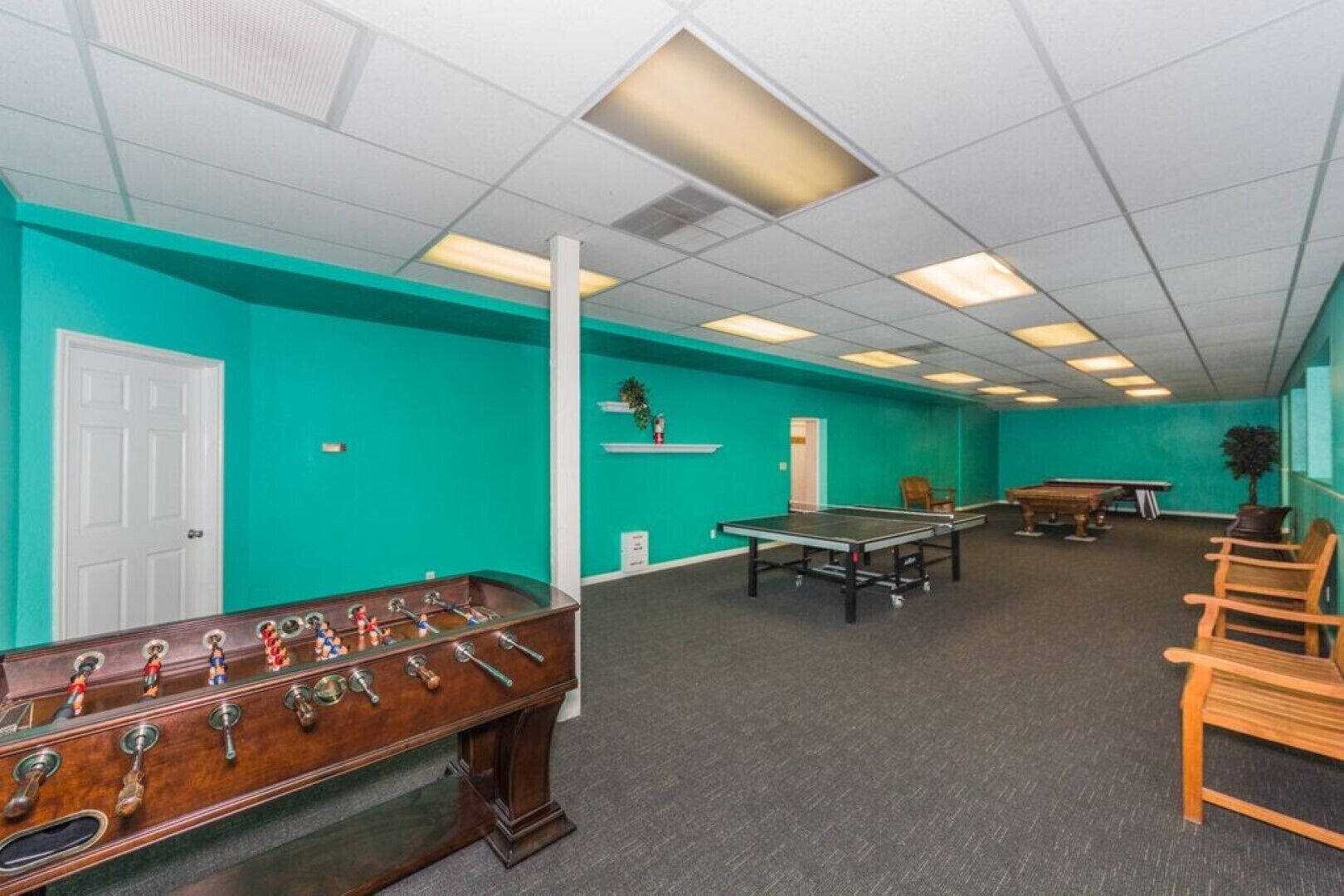 A room with teal walls, a foosball table, a ping pong table, and a pool table.