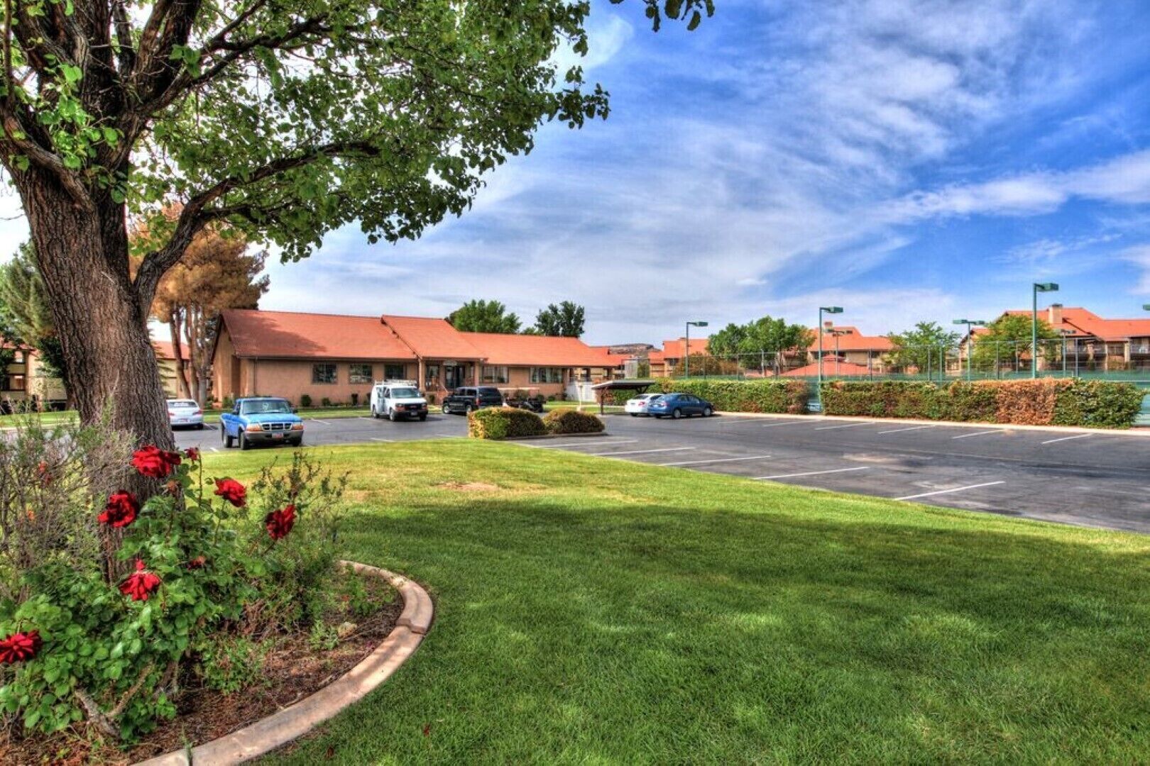 A hotel with a parking lot, a building with a red roof, and a tree with red flowers.