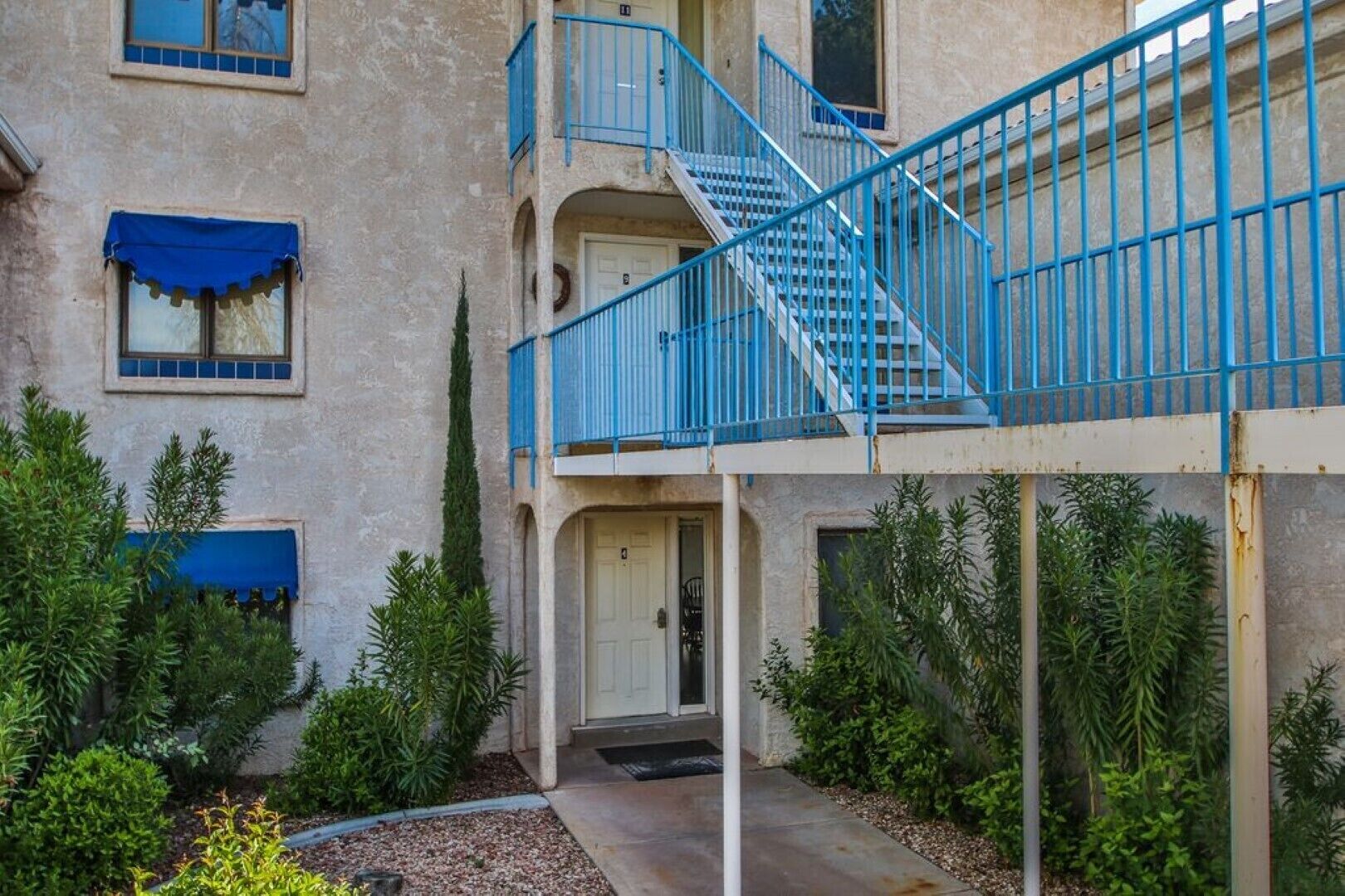 A multi-story building with a central staircase, balconies, and a small garden area with shrubs and a pathway.