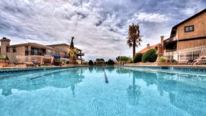 Una piscina con agua azul cristalina, rodeada de edificios con balcones y palmeras.