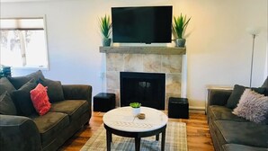 Una sala de estar con chimenea, dos sofás, una mesa de centro y un televisor de pantalla plana montado sobre la chimenea.