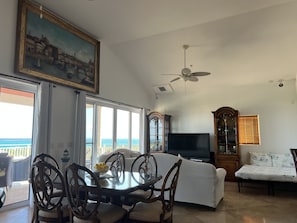 A living room with a dining table, chairs, a sofa, a TV, and a large window with a view of the ocean. - ParadiseNest Penthouse Million Dollar OceanViews-GraceBay Beach-Central Location (Providenciales)