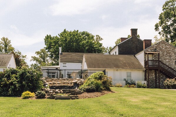 A traditional brick house with a stone staircase leading to a white door, surrounded by a well-maintained lawn and a small garden with various plants. - Historic Belle Air Mansion (Nashville)