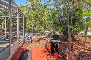 A patio area with a barbecue grill, outdoor seating, and a glass-enclosed structure.