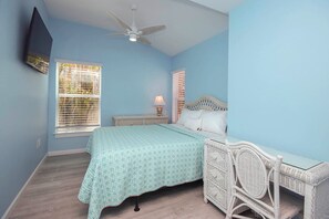 A bedroom with a bed, a nightstand, a lamp, a ceiling fan, and a TV mounted on the wall.