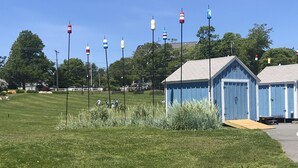 A grassy area with a wooden boardwalk, a blue building with a door, and several colorful buoys. - Townhouse-Beach Vacation at the Yachtsman in Hyannis (Barnstable)