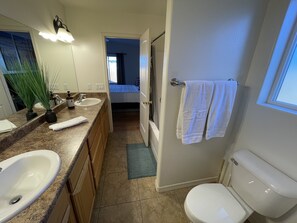 Un baño con dos lavamanos, un inodoro, una ducha y una puerta que da a un dormitorio.