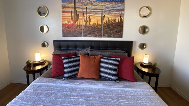 Une chambre à coucher avec un lit, un grand tableau représentant des cactus et plusieurs miroirs ronds accrochés aux murs.