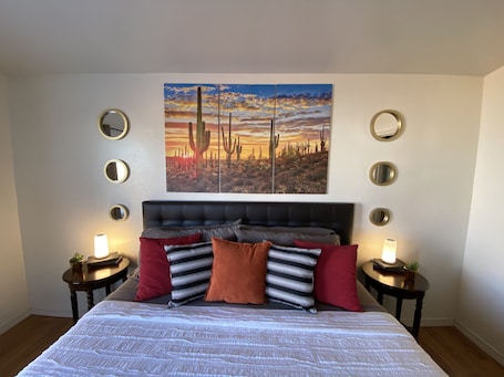 A bedroom with a bed, a large painting of cacti, and multiple round mirrors on the walls.