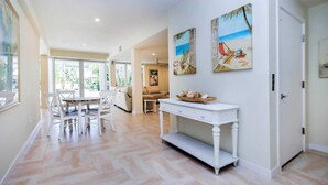 A spacious living area with a dining table and chairs, a white console table with decorative items, and a view of the outdoors through large windows. - Spacious 5BR Captiva Retreat with Private Pool, Spa & Game Room (Captiva)