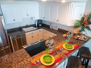 A kitchen with white cabinets, a granite countertop, a sink, a coffee maker, and a decorative sign.