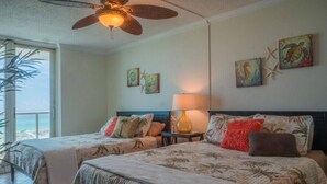 Une chambre avec deux lits, un ventilateur de plafond, une lampe et des œuvres d’art accrochées au mur.