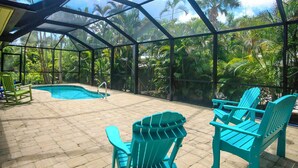 A covered outdoor area with a pool, chairs, and tropical plants. - Colorful 4BR Captiva Village Retreat with Private Heated Pool (Captiva)