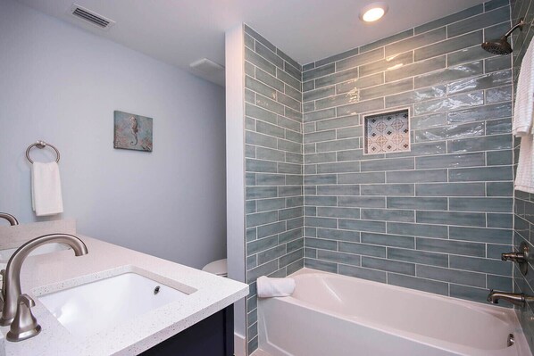 Une salle de bain avec un lavabo blanc, une baignoire et une douche dotée d’un pommeau de douche à effet pluie.