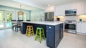 A modern kitchen with white cabinets, stainless steel appliances, and a large island with stools. - Colorful 4BR Captiva Village Retreat with Private Heated Pool (Captiva)