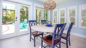 A dining area with a round table, six chairs, and a hanging light fixture. - Colorful 4BR Captiva Village Retreat with Private Heated Pool (Captiva)