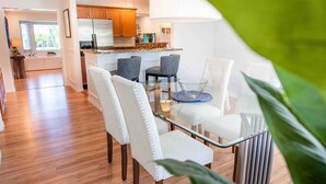 Een moderne keuken met houten kastjes, een koelkast, en een eethoek met een glazen tafel en witte stoelen.
