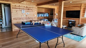 Een kamer met een tafeltennistafel, een bank, een televisie en een tafelvoetbaltafel.