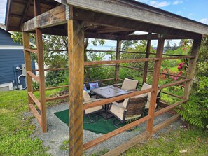 A wooden pergola with a table and chairs, surrounded by greenery and a view of the outdoors. - Mountain and Sound view, kid/dog/game-friendly (Freeland)