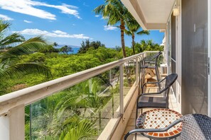 Ein Balkon mit Glasgeländer, zwei Korbstühle und einem kleinen Tisch.