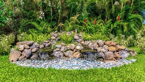 Ein Garten mit einem kleinen Wasserfall, umgeben von Felsen und üppigem Grün.