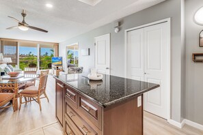 A kitchen with a granite countertop, wooden cabinets, and a dining area with wicker chairs.
