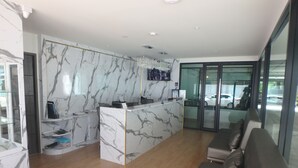 A modern reception area with a marble reception desk, a seating area with leather sofas, and a glass door leading outside. - Donmueang Place Hotel (Bangkok)