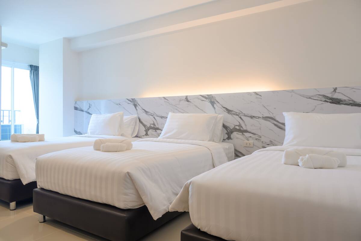 Habitación de hotel con tres camas, cada una con ropa blanca y almohadas, y cabecera con estampado de mármol.