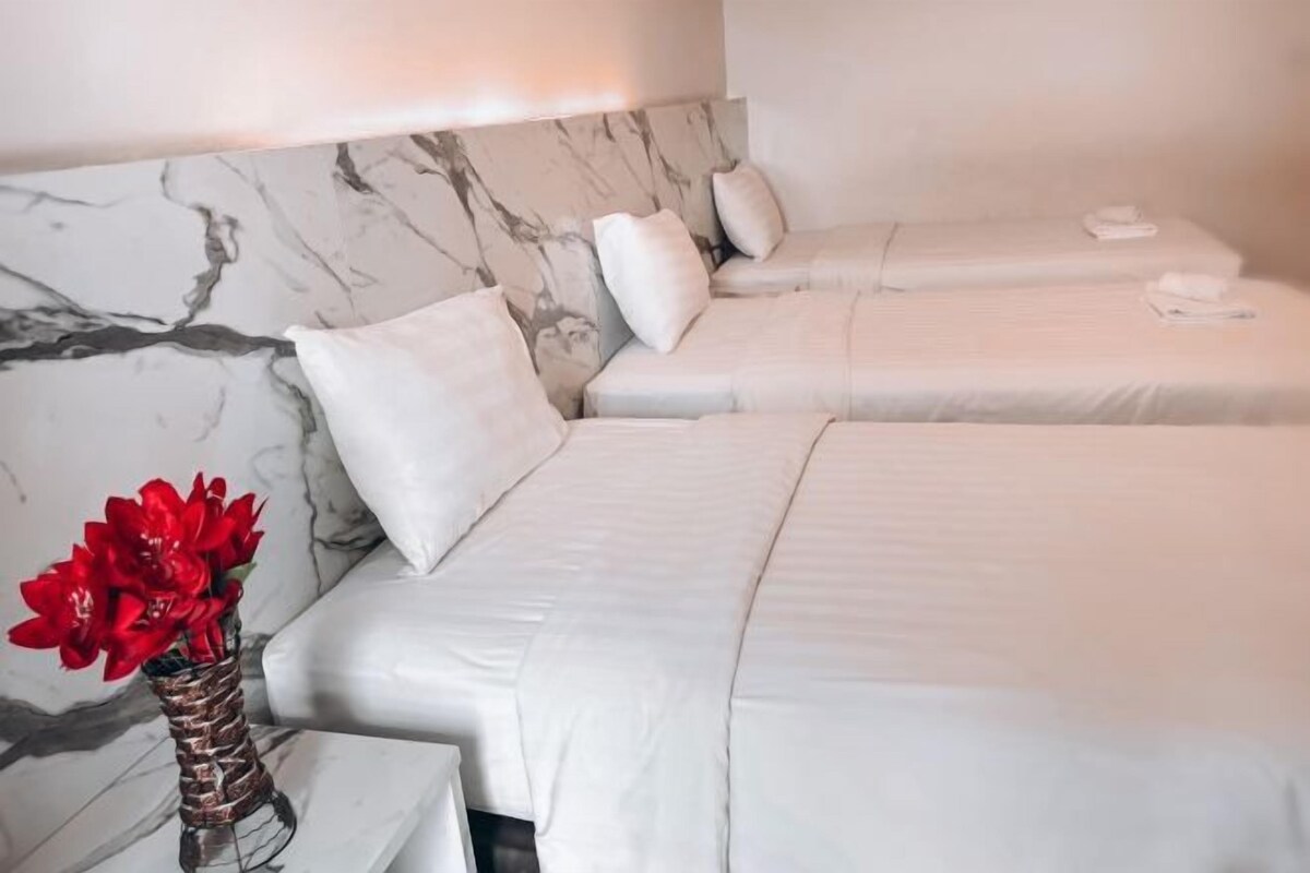 Ett hotellrum med två sängar, ett sänggavel i marmor, vita sängkläder och en vas med röda blommor.