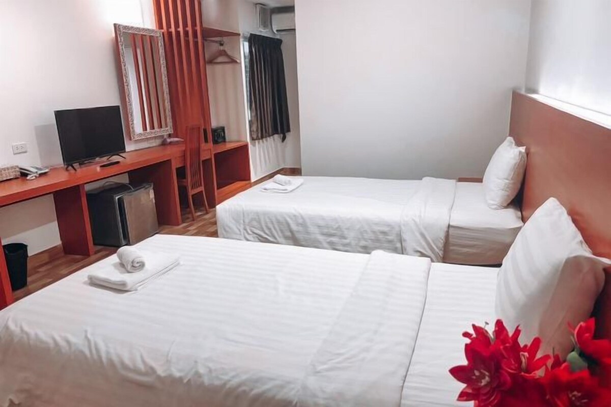 Ein Hotelzimmer mit zwei Betten, einem Schreibtisch mit Computer, einem Fernseher und einem Kleiderschrank.