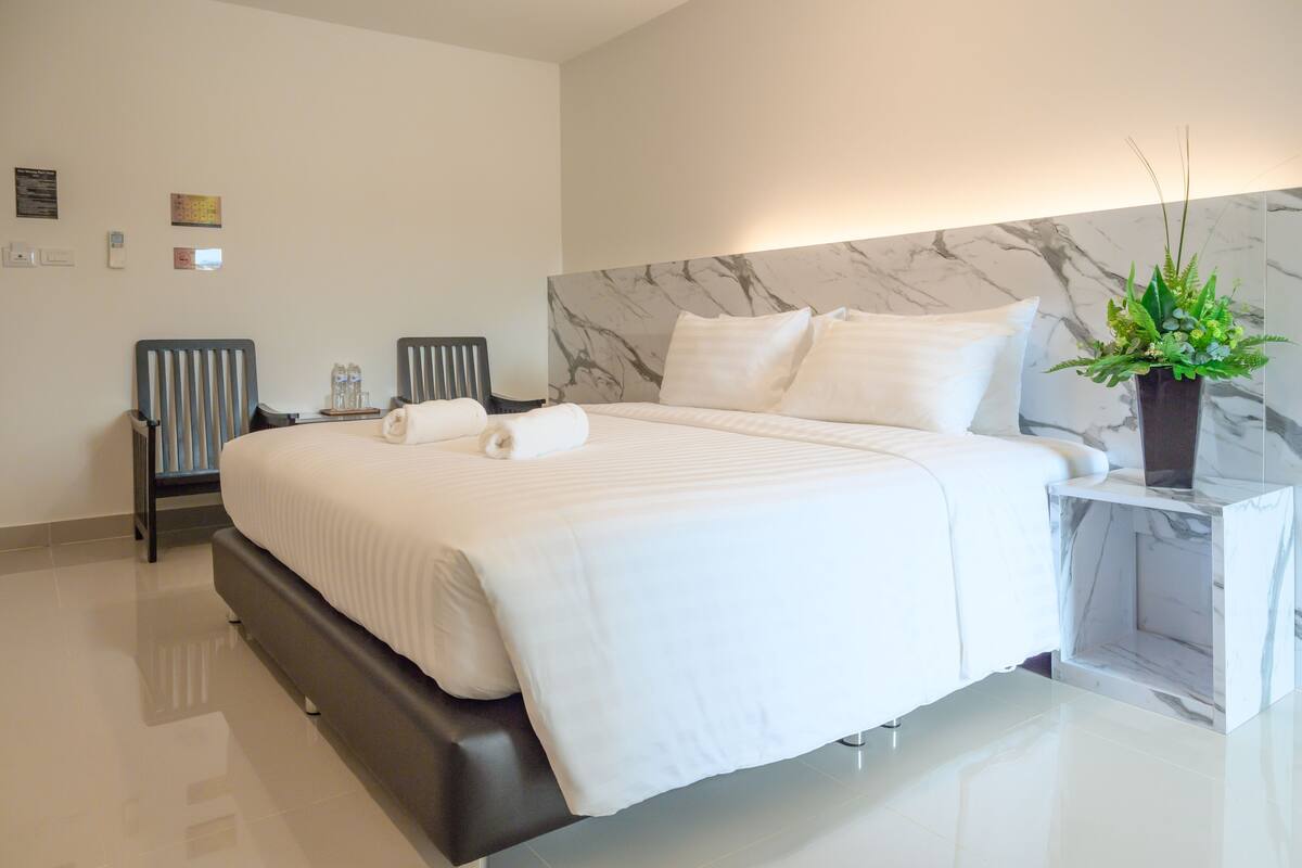 Una habitación de hotel moderna con una cama grande, cabecera de mármol, mesita de noche con una planta y una lámpara de pared.