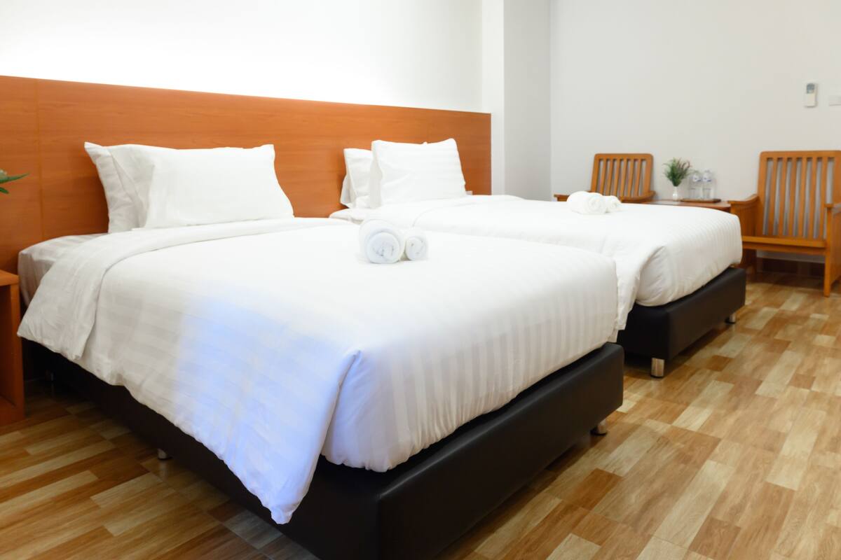 Una habitación de hotel con dos camas, cabecero de madera, suelo de madera y una mesita con una planta.