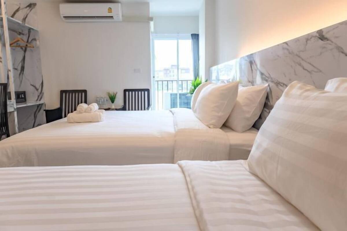 Habitación de hotel con dos camas, cabecera de mármol, unidad de aire acondicionado y vistas a la ciudad desde la ventana.