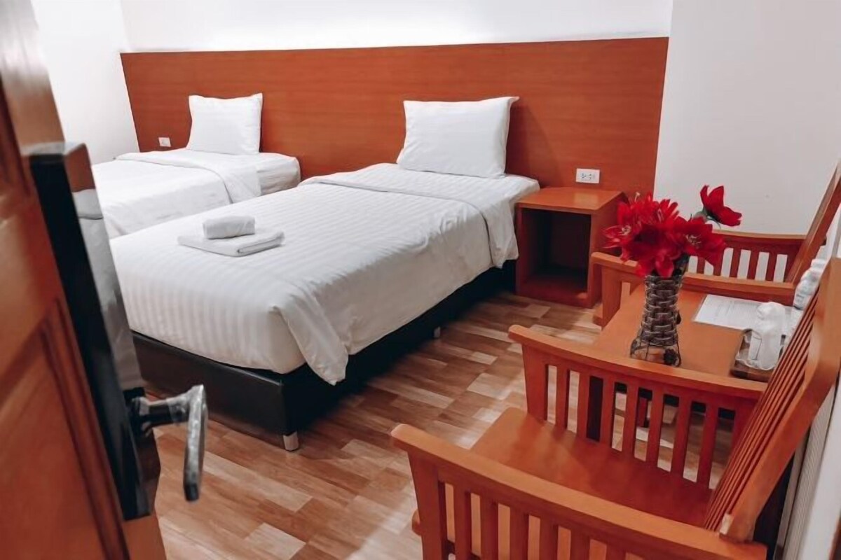 Habitación de hotel con dos camas, un cabecero de madera, una mesita con un florero y una silla.