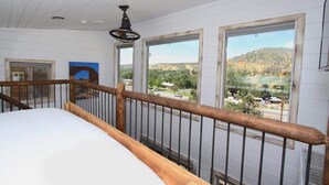 Un dormitorio con cama de madera, ventilador de techo y ventanas amplias con vista a la montaña.