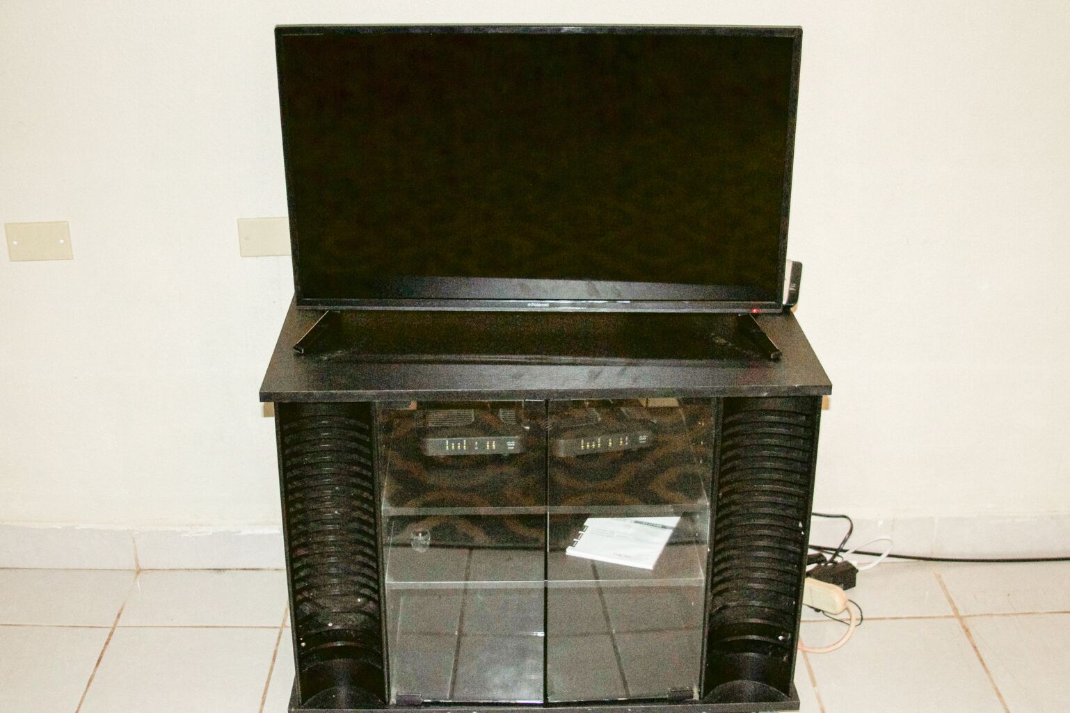 A black entertainment unit with a flat-screen TV, a control panel, and a glass-fronted cabinet.