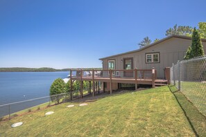 Una casa con terraza con vista a un lago, un patio cercado y cielo despejado.