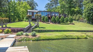 A lakeside property with a wooden dock, a house with a deck, and a well-maintained lawn.