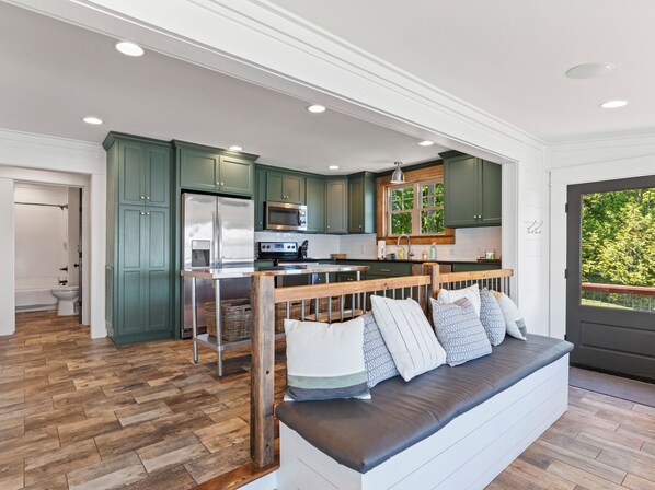 A modern kitchen with green cabinets, stainless steel appliances, and a wooden dining area.