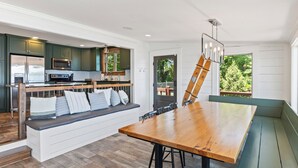 A modern kitchen with dark green cabinets, stainless steel appliances, and a wooden bench with cushions.