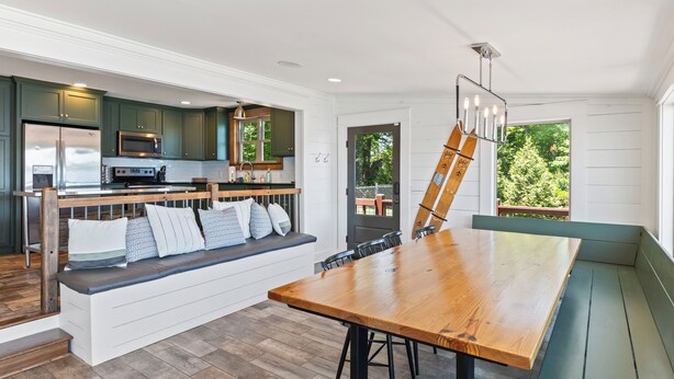 A modern kitchen with dark green cabinets, stainless steel appliances, and a wooden bench with cushions.