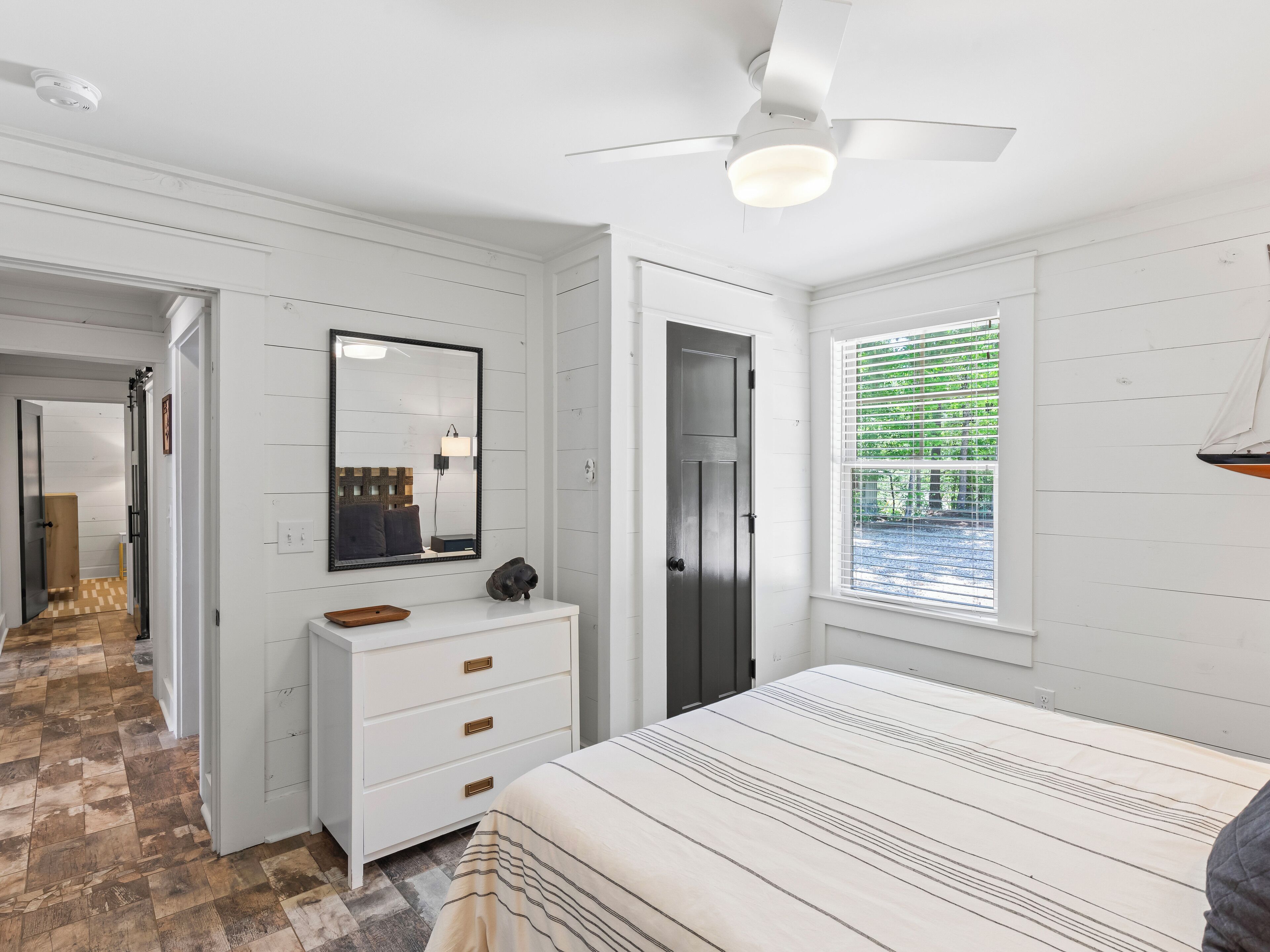 A bedroom with a bed, a dresser, a mirror, a ceiling fan, and a window with blinds.