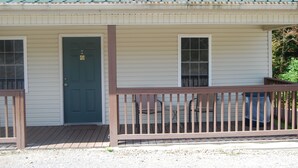 Un bâtiment d’un seul étage, doté d’un toit métallique vert, d’une porte d’entrée sur laquelle est apposé un panneau indiquant « Stationnement interdit », et d’une terrasse en bois avec des chaises.