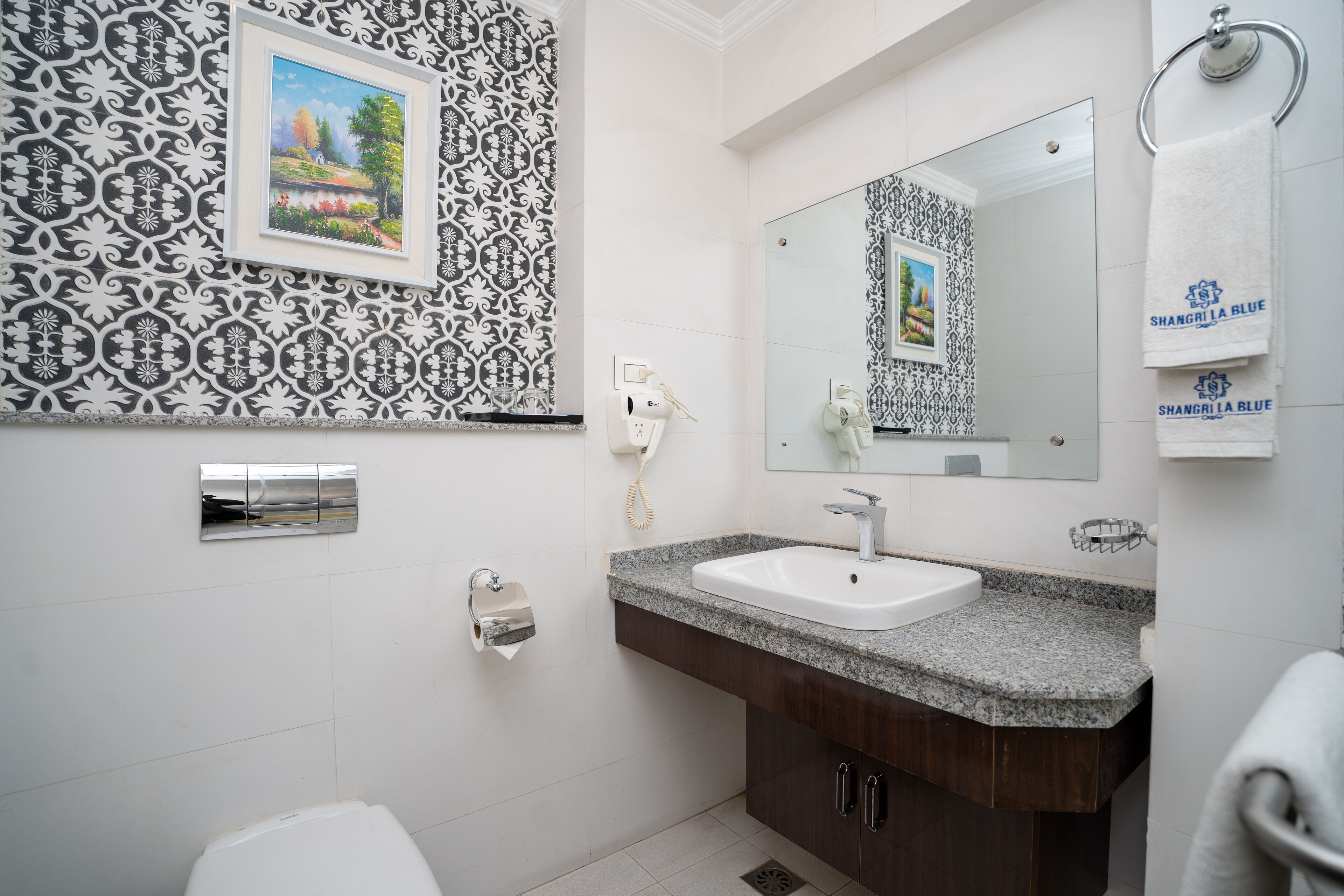 Un baño con lavamanos blanco, tocador de madera oscura, un espejo grande y azulejos de pared estampados.
