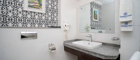 Un baño con lavamanos blanco, tocador de madera oscura, un espejo grande y azulejos de pared estampados.