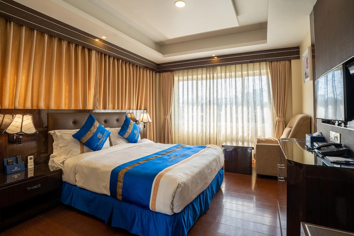 A hotel room with a large bed, a desk, a chair, and a television.