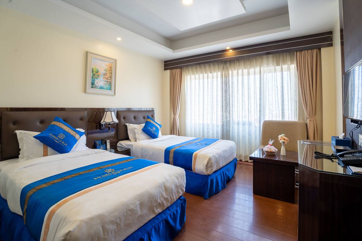 A hotel room with two beds, a desk, and a chair.