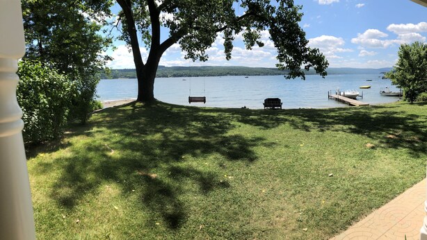 A grassy area with a bench and a swing under a tree, overlooking a lake with boats and a dock. - Year round lakefront house on Keuka Lake (Hammondsport)
